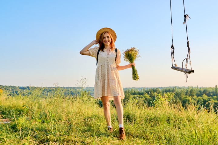 Happy smiling adult woman in dress with hat bouquet of wildflowers. Middle-aged female in summer meadow with wild grasses. Nature, beauty, fashion, joy, health, happiness, people 40s of age concept